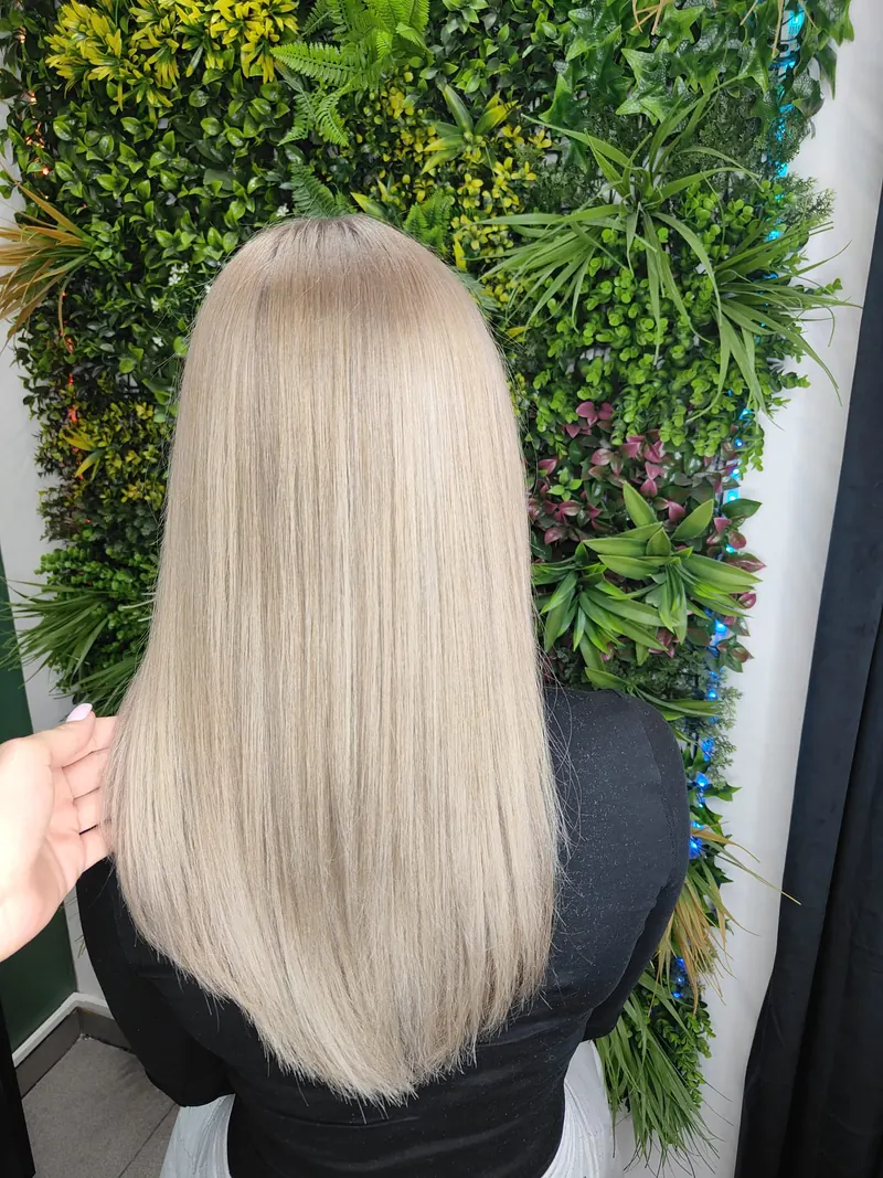 Długie proste blond włosy na tle ściany roślin i zielonych światełek w salonie Jowity Litwin